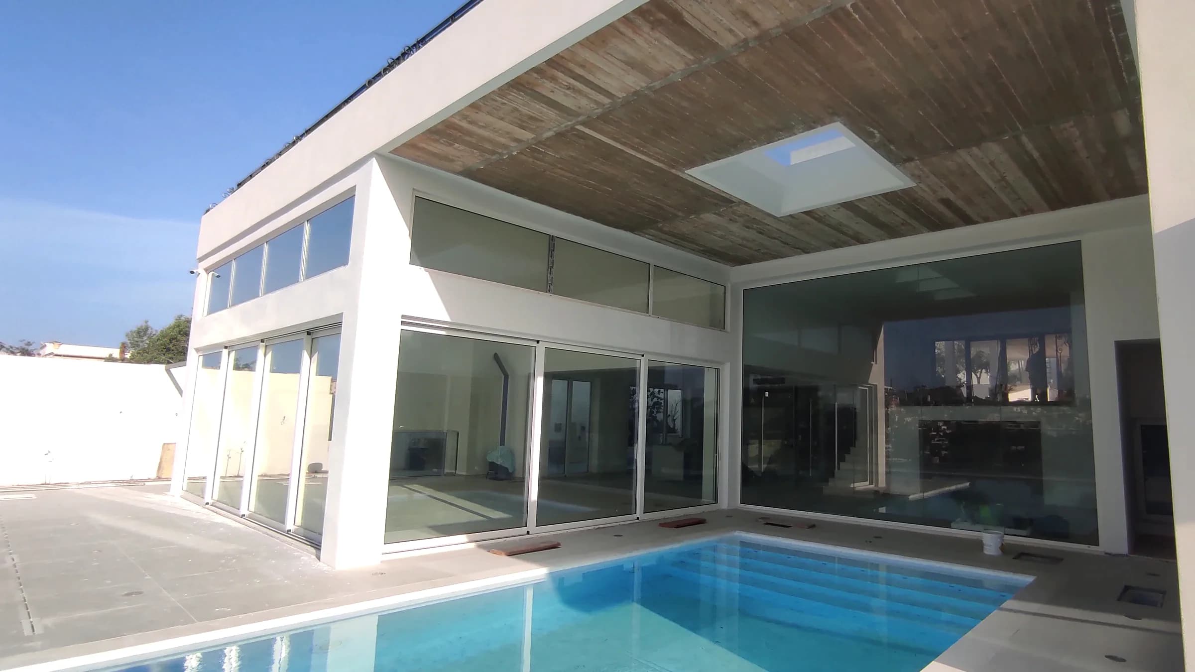 Villa pool leading to a glazed living space beneath a concrete soffit